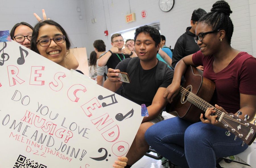 Priyal Garg, 12, holds the poster for Crescendo as Adaeze Njoku plays the guitar and Josh Redona sings along. Students with a love for music can perform and express themselves in Crescendo.