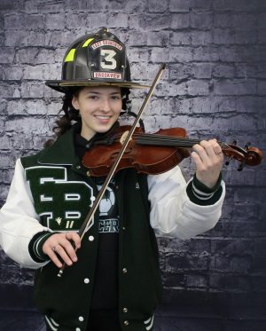Kaleigh Duffy smiles, showing off her fire helmet, varsity jacket, AND violin, demonstrating her multitude of interests.