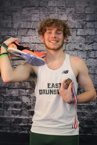 Senior Vinny Taormina flashes a proud smile as he holds his track spikes in one hand and a medal in another.